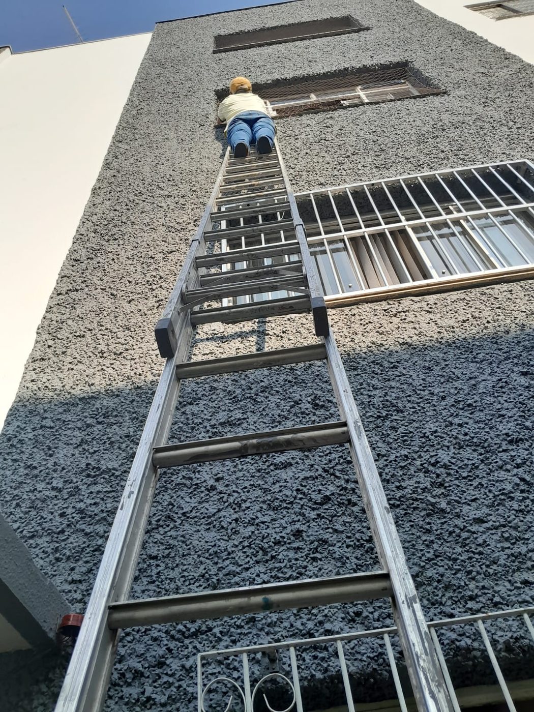 Pintor na escada trabalhando na fachada de um prédio com parede texturizada