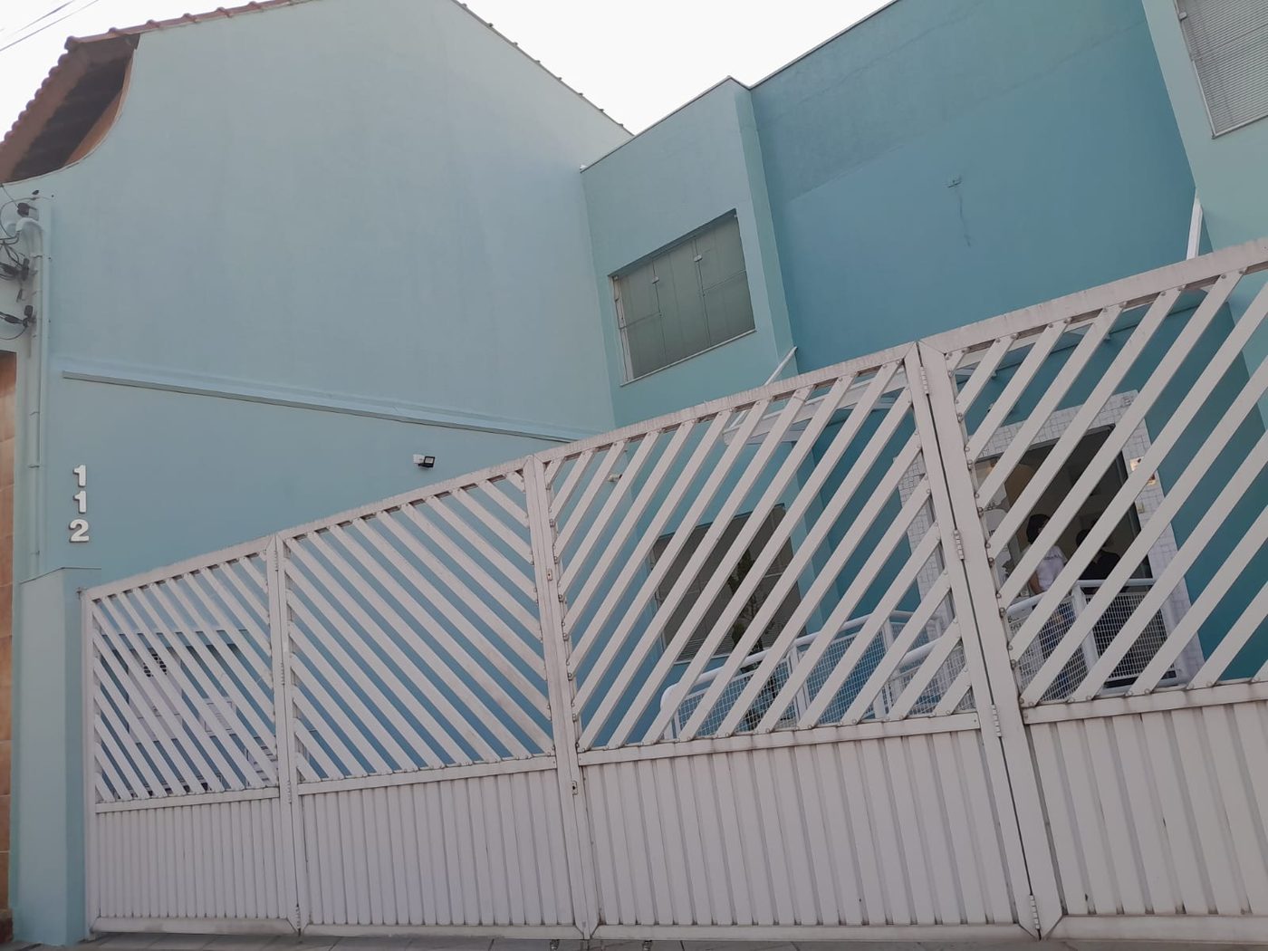 Sobrado com a fachada pintada em azul claro, com portão branco na frente